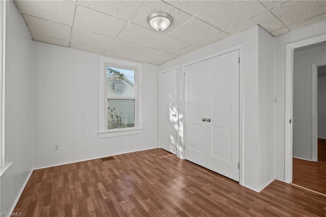 unfurnished bedroom with a paneled ceiling, wood finished floors, and visible vents