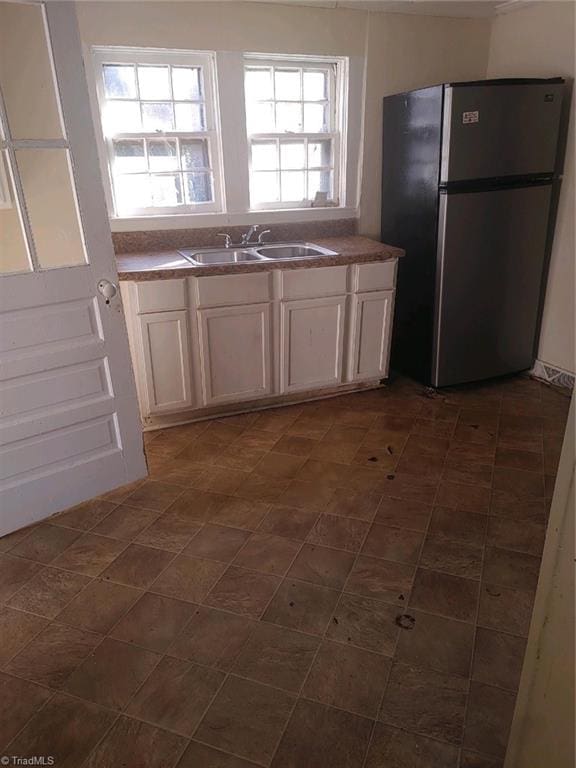 kitchen featuring sink, dark tile patterned floors, white cabinets, and stainless steel fridge