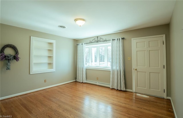 spare room with built in shelves, baseboard heating, and light hardwood / wood-style flooring