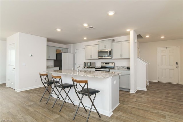 kitchen featuring visible vents, a kitchen island with sink, wood finished floors, appliances with stainless steel finishes, and a breakfast bar area