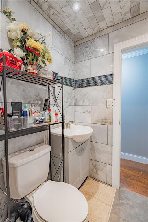 half bath featuring toilet, tile walls, baseboards, wood finished floors, and vanity