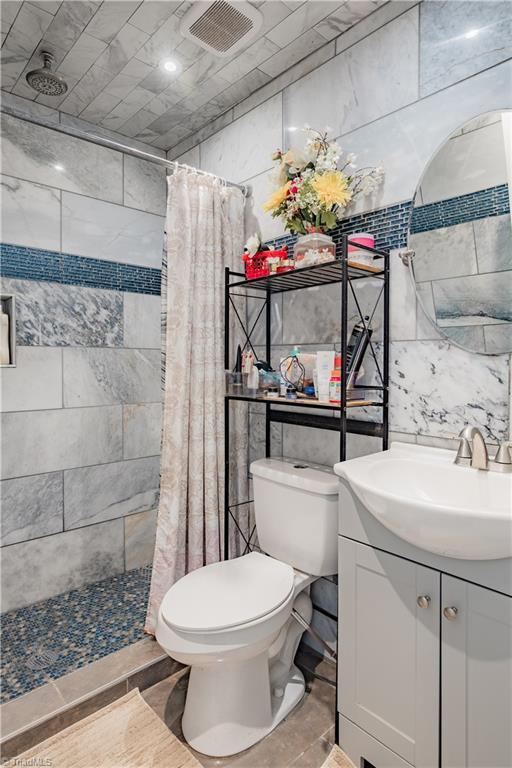 bathroom with tile walls, toilet, visible vents, and a tile shower