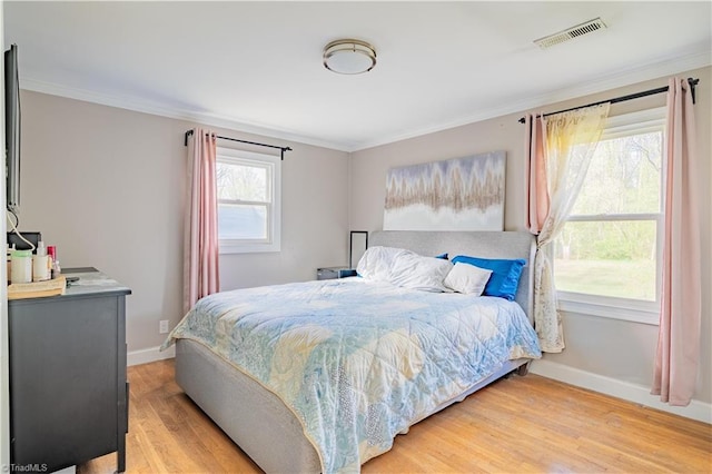 bedroom featuring baseboards, light wood-style flooring, visible vents, and ornamental molding