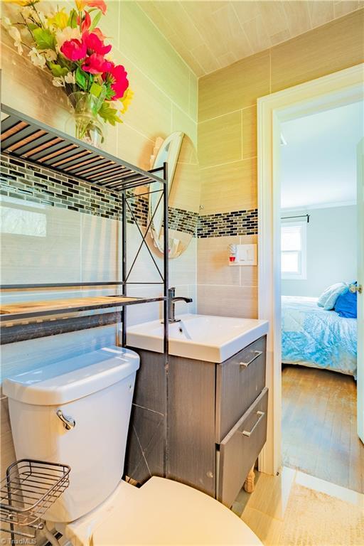 bathroom featuring wood finished floors, toilet, vanity, connected bathroom, and tile walls