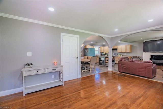 living room featuring arched walkways, wood finished floors, ornamental molding, and recessed lighting