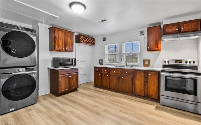 kitchen featuring light wood-type flooring, stainless steel electric range oven, sink, and stacked washer and clothes dryer