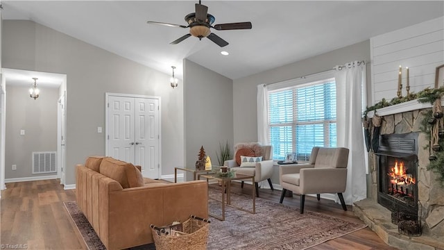 sitting room with a stone fireplace, ceiling fan, wood-type flooring, and lofted ceiling