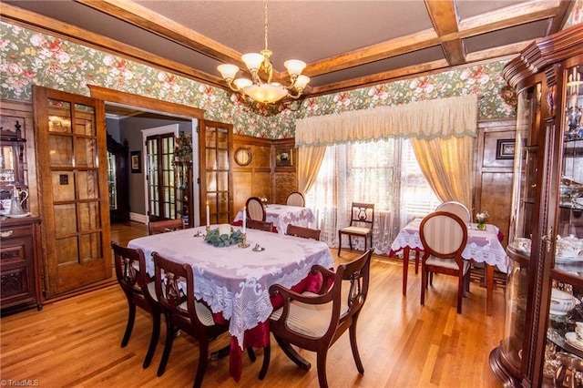 dining room featuring light hardwood / wood-style flooring, crown molding, an inviting chandelier, and coffered ceiling