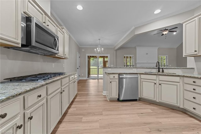 kitchen featuring appliances with stainless steel finishes, a sink, a chandelier, ceiling fan, and light wood finished floors