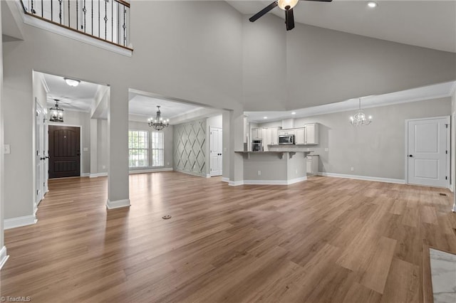 unfurnished living room featuring a chandelier, ceiling fan, light wood-type flooring, baseboards, and high vaulted ceiling
