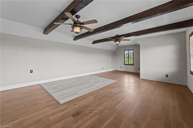 unfurnished living room with a ceiling fan, brick wall, wood finished floors, baseboards, and beamed ceiling