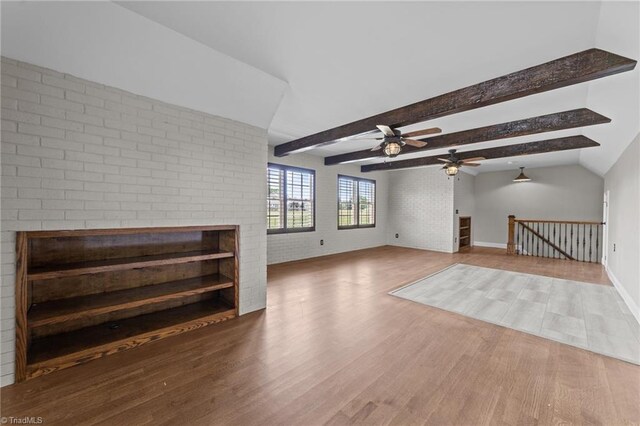 unfurnished living room featuring wood finished floors, a ceiling fan, a fireplace, brick wall, and baseboards
