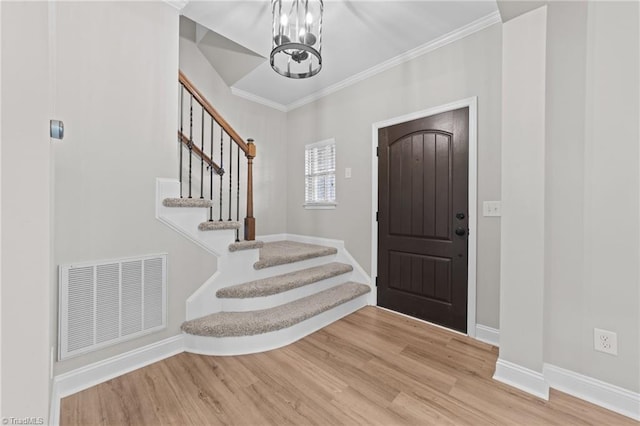 foyer featuring a chandelier, stairs, wood finished floors, crown molding, and baseboards