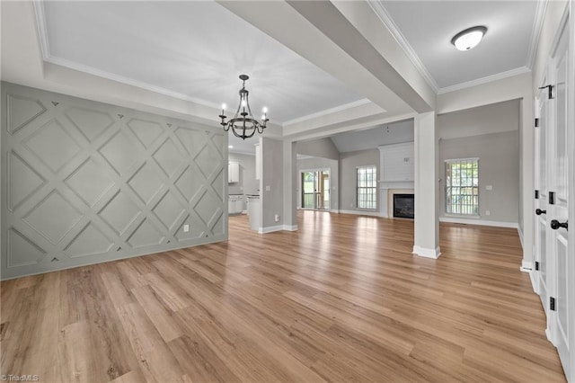 unfurnished living room featuring light wood-style floors, a chandelier, a fireplace, crown molding, and a decorative wall