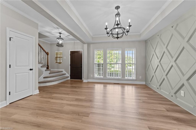foyer featuring a chandelier, light wood finished floors, stairs, a raised ceiling, and baseboards