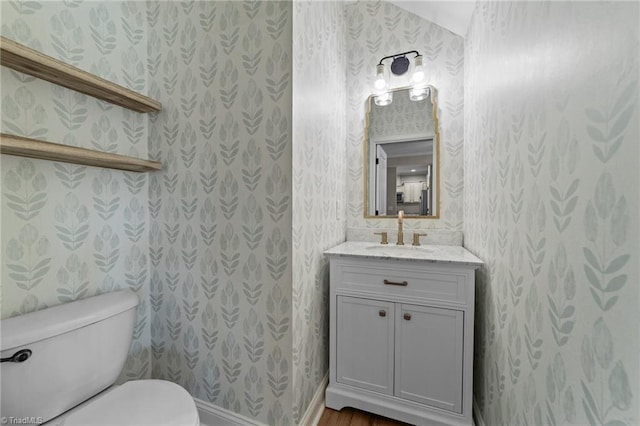 half bathroom with wallpapered walls, toilet, and vanity