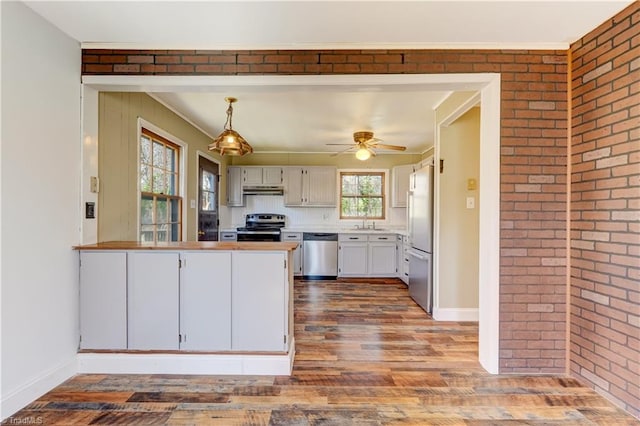 kitchen with under cabinet range hood, appliances with stainless steel finishes, a peninsula, and brick wall