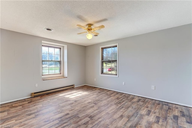 spare room featuring visible vents, a textured ceiling, wood finished floors, baseboard heating, and ceiling fan