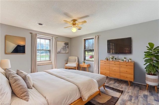 bedroom featuring visible vents, a textured ceiling, wood finished floors, and a ceiling fan