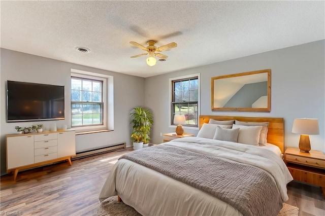 bedroom with a ceiling fan, wood finished floors, visible vents, a textured ceiling, and a baseboard heating unit