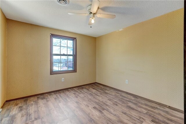 empty room featuring wallpapered walls, ceiling fan, wood finished floors, and a textured ceiling