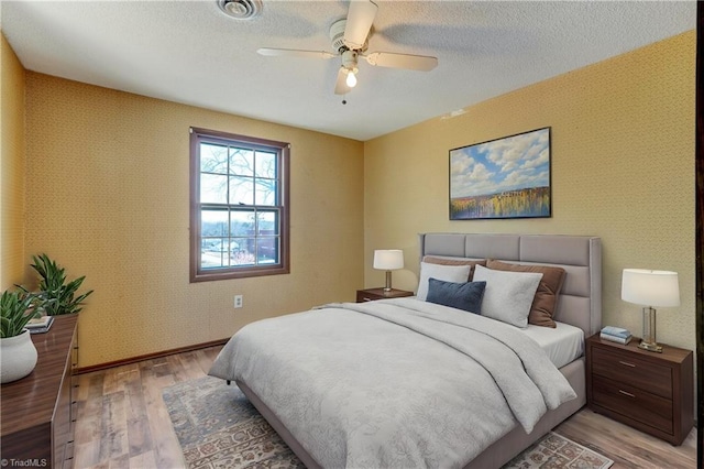 bedroom featuring light wood-style flooring, a textured ceiling, and wallpapered walls