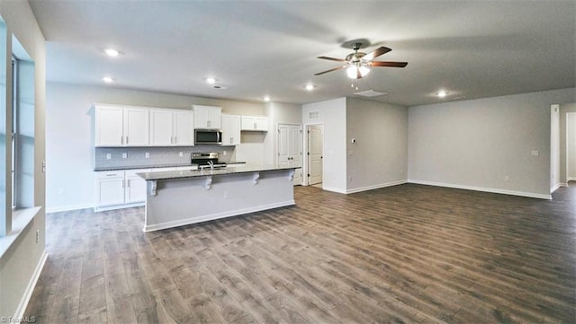 kitchen with a kitchen bar, an island with sink, stainless steel appliances, decorative backsplash, and white cabinets