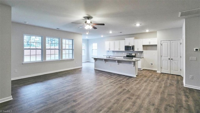 kitchen with dark wood-type flooring, white cabinetry, stainless steel appliances, a kitchen breakfast bar, and a center island with sink