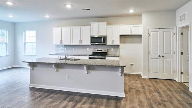 kitchen with dark stone countertops, white cabinets, a kitchen bar, a kitchen island with sink, and stainless steel appliances