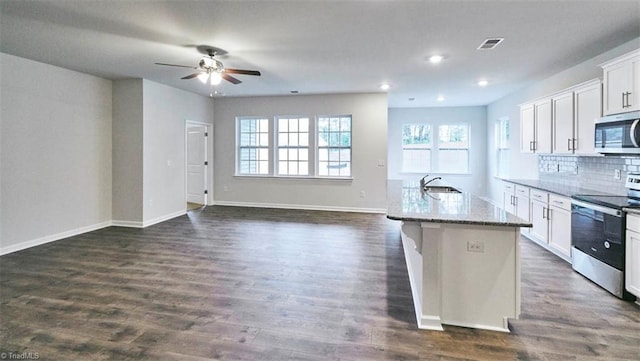 kitchen with appliances with stainless steel finishes, sink, white cabinets, a kitchen island with sink, and light stone countertops