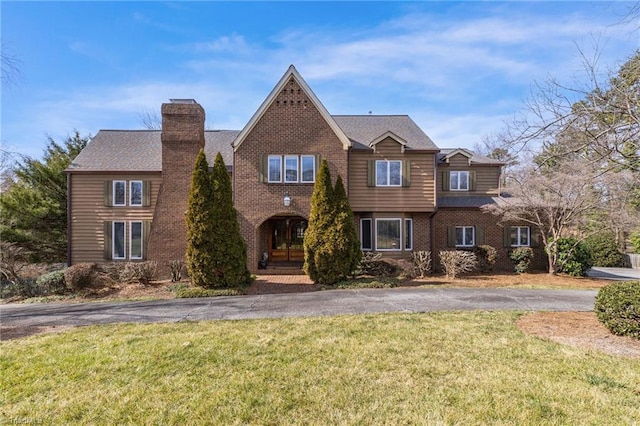 view of front of house with a front yard, a chimney, and brick siding