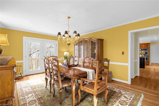 dining space with ornamental molding, wood finished floors, french doors, and an inviting chandelier