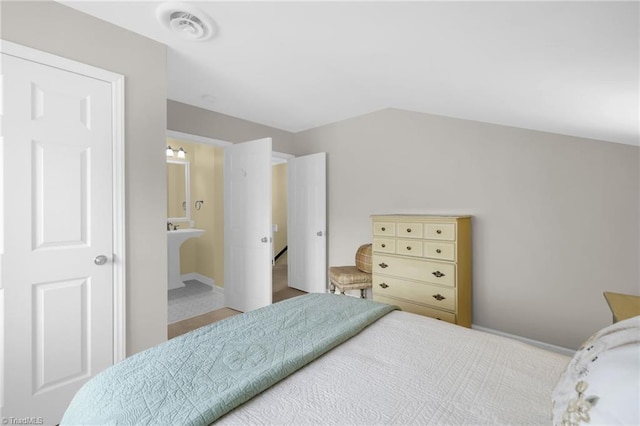 bedroom with lofted ceiling, visible vents, and ensuite bath