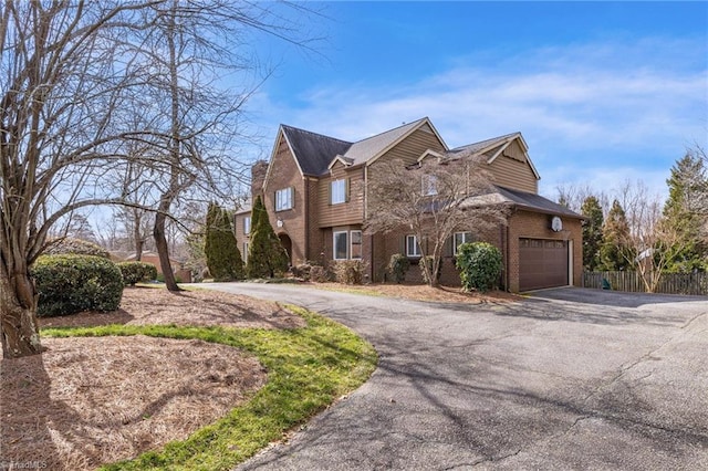 traditional-style home featuring a garage, driveway, brick siding, and fence