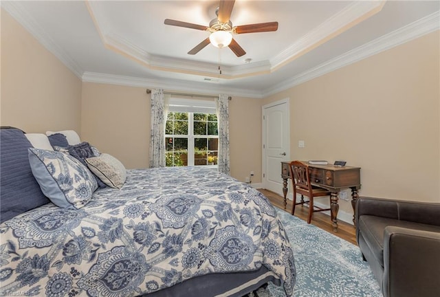 bedroom with a tray ceiling, ornamental molding, ceiling fan, wood finished floors, and baseboards