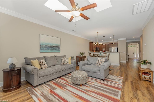 living area with light wood-type flooring, a skylight, arched walkways, and crown molding