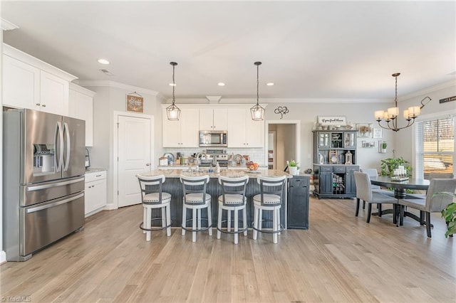 kitchen with appliances with stainless steel finishes, white cabinets, a kitchen island with sink, and pendant lighting