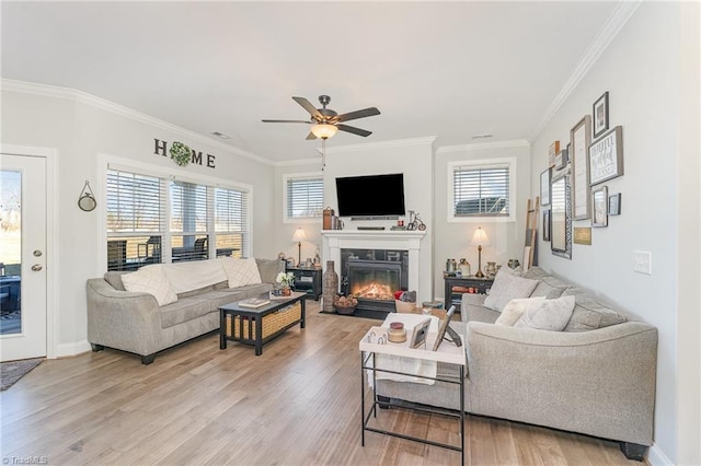 living room with crown molding, wood finished floors, a wealth of natural light, and a glass covered fireplace