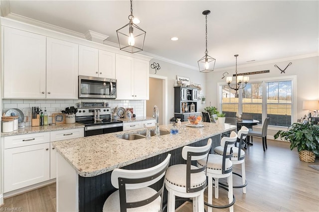 kitchen with stainless steel appliances, a kitchen island with sink, a sink, and white cabinetry