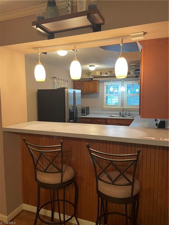 kitchen featuring brown cabinetry, a peninsula, light countertops, stainless steel refrigerator with ice dispenser, and a sink