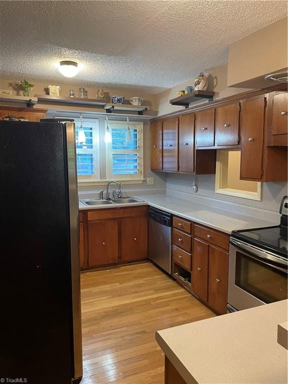 kitchen with stainless steel appliances, a sink, light countertops, light wood finished floors, and brown cabinetry