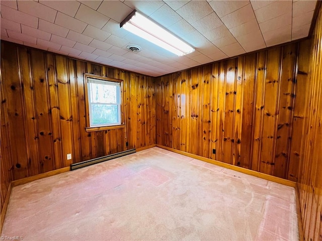 carpeted spare room with a baseboard heating unit and wooden walls