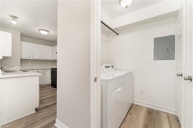 washroom with electric panel, independent washer and dryer, light wood-type flooring, and sink