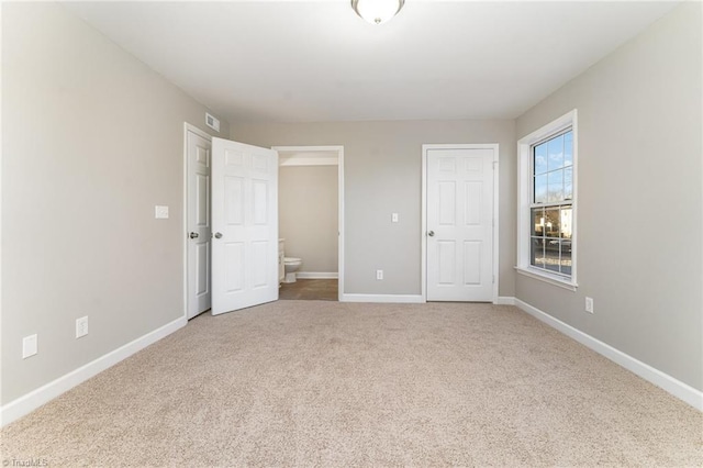 unfurnished bedroom featuring ensuite bath and carpet flooring