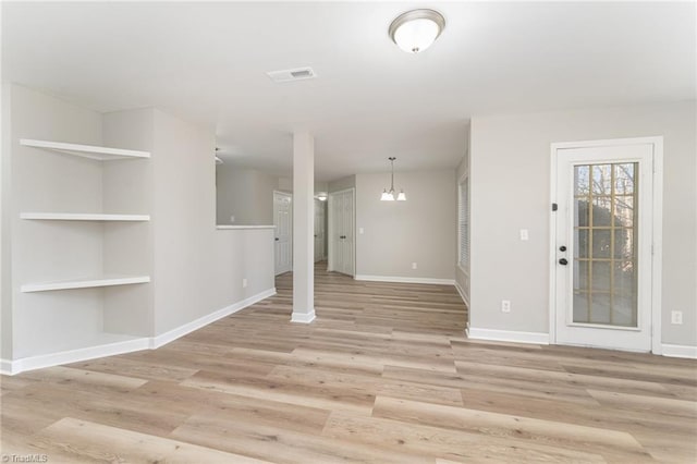 interior space with built in shelves, a notable chandelier, and light hardwood / wood-style flooring