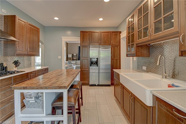 kitchen with stainless steel refrigerator with ice dispenser, gas stovetop, a sink, decorative backsplash, and wall chimney exhaust hood