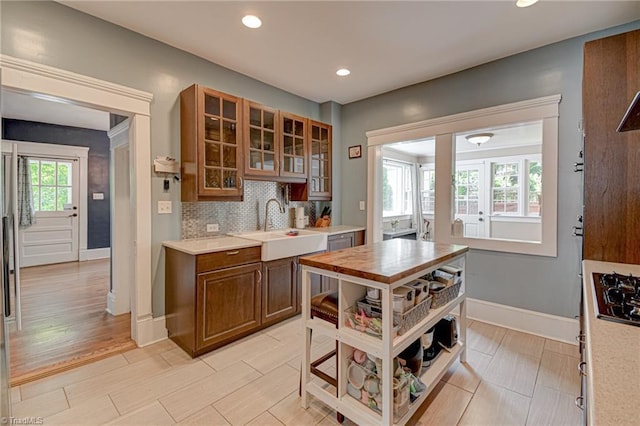 kitchen with a sink, light countertops, backsplash, glass insert cabinets, and recessed lighting