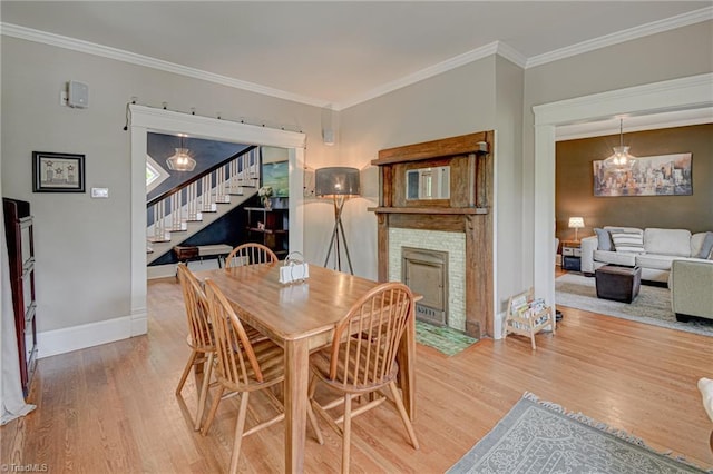 dining space featuring stairs, a fireplace with flush hearth, light wood-style floors, baseboards, and crown molding