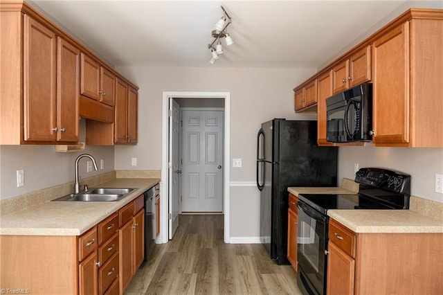 kitchen with light wood-type flooring, black appliances, light countertops, and a sink