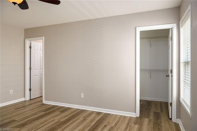 unfurnished bedroom featuring wood finished floors, multiple windows, a closet, and a walk in closet